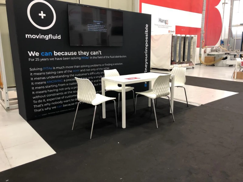 allestimento-con-tappeto-e-parete-nera-e-tavoli-e-sedie-uni-bianche