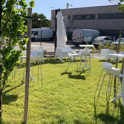 area-relax-esterna-con-tavolini-alti-e-sgabelli-easy-bianchi-su-un-prato-verde