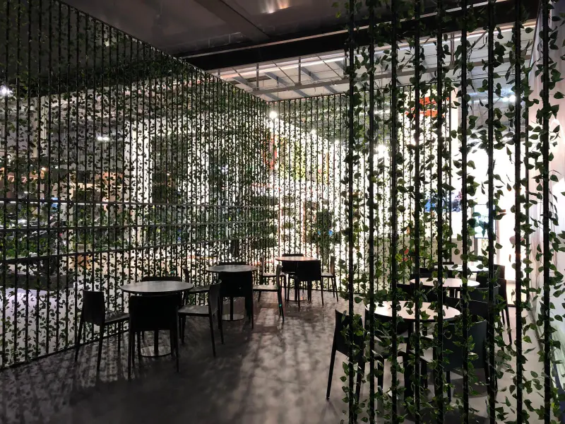 divisori-modulari-ricoperti-di-piante-rampicanti-attorno-alla-zona-bar-con-tavoli-e-sedie-neri