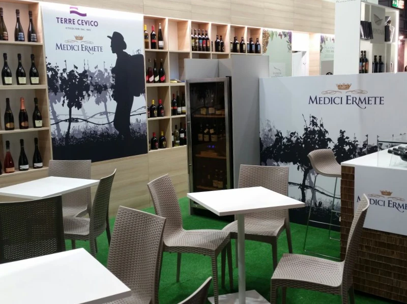 stand-con-erba-sintetica-vini-esposti-tavolini-bianchi-e-sedie-grige-bistrot